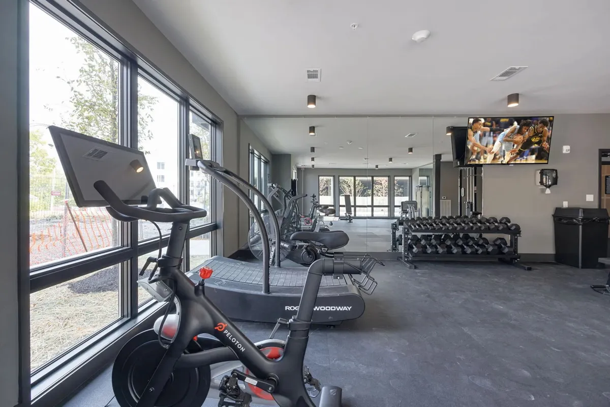 A state-of-the-art fitness center featuring a Peloton bike, treadmill, free weights, a large-screen TV, and expansive windows that bring in natural light. The space is modern, motivating, and suitable for both group classes and solo workouts.