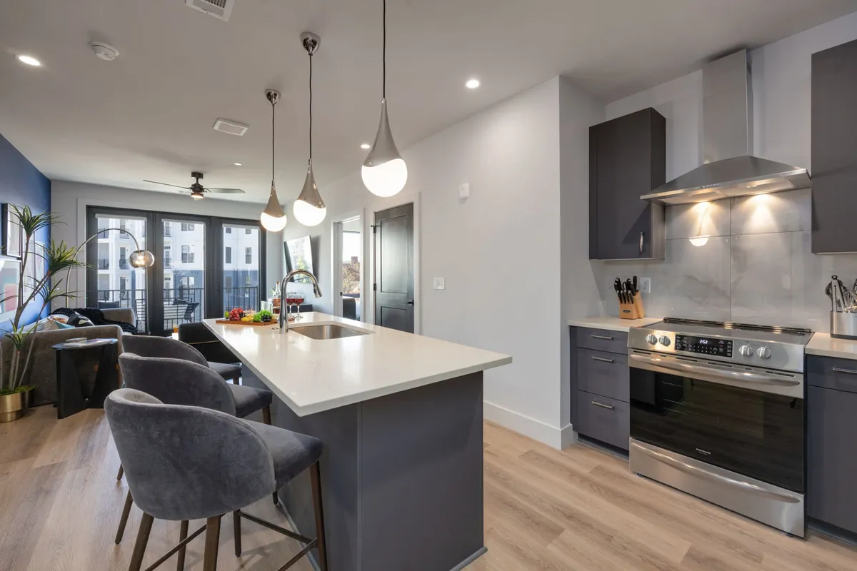 A contemporary kitchen with an island countertop, modern stainless steel appliances, a comfortable seating area, and large windows letting in plenty of natural light. The setup is ideal for both meal prep and relaxed group gatherings.