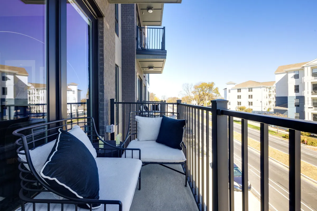 A stylish condo balcony with comfortable seating overlooks a bustling urban street. The view captures surrounding buildings, hinting at the walkability and lively atmosphere of the neighborhood, perfect for sunset relaxation or morning coffee breaks.