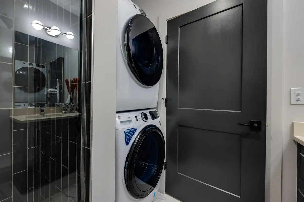A contemporary laundry area featuring a washer and dryer set, a dark modern door, and a practical countertop, all designed for efficiency and simplicity.