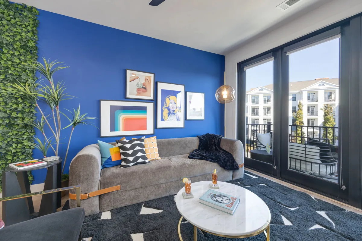 A cozy living room showcasing a sofa adorned with colorful cushions, a coffee table with decorative items, and large windows offering outdoor views. The contemporary atmosphere is perfect for both relaxation and accommodating extra guests on the sleeper sofa.
