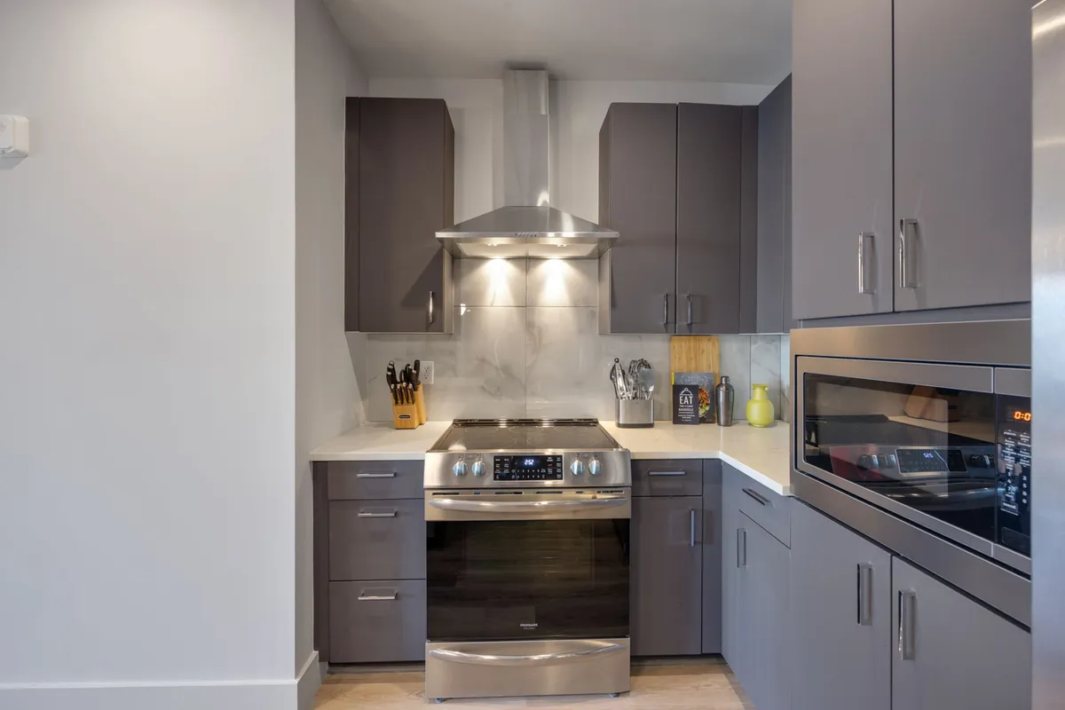 A detailed view of a kitchen featuring a stainless steel stove, sleek cabinetry, a modern hood range, and extensive countertop workspace. The efficient layout is perfect for enthusiastic cooks and group meal prep.