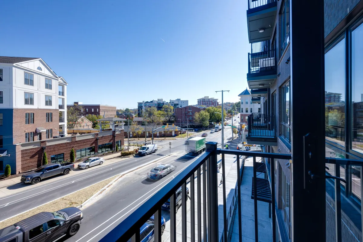 A private balcony with a sleek railing overlooks the lively city street below, surrounded by neighboring buildings that hint at the energy and vibrancy of Midtown. The urban landscape is alive with the activity of people and local businesses, perfect for sunset views and people-watching.